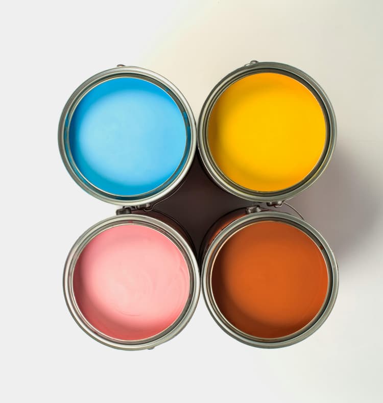 Vier offene Farbdosen stehen eng beieinander und bilden ein Quadrat. Die Farben sind Hellblau, Gelb, Rosa und Braun. Die Farbdosen sind von oben fotografiert, sodass die glatten, glänzenden Oberflächen der Farbe sichtbar sind. Der Hintergrund ist einfarbig und hell.